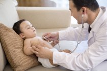Médico chino escuchando latidos del corazón del niño bebé - foto de stock
