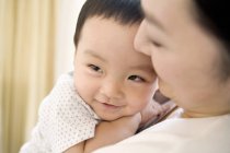 Chinese woman holding infant on chest and smiling — Stock Photo