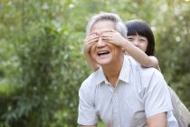 Китаянка закрывает дедушкины глаза руками в саду — стоковое фото