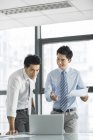 Empresarios chinos usando portátil y hablando en la oficina - foto de stock