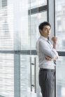 Китайский бизнесмен стоит у окна и смотрит в камеру — стоковое фото