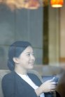 Mujer de negocios china sentada con teléfono inteligente en la cafetería - foto de stock