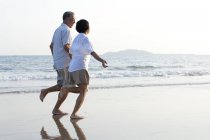 Senior pareja china corriendo en la playa de arena - foto de stock