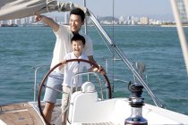 Padre e hijo chinos navegando en yate en la bahía - foto de stock