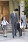 Китайская деловая пара с детьми, идущими рука об руку на улице — стоковое фото