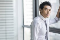Homem de negócios chinês em pé à janela e olhando para a câmera — Fotografia de Stock