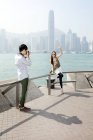 Chinese man taking picture of young woman with camera in Victoria Harbor, Hong Kong — Stock Photo