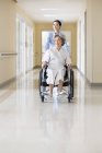 Infermiera cinese spingendo donna anziana in sedia a rotelle — Foto stock