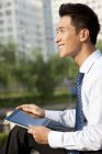 Китайский бизнесмен сидит с цифровым планшетом в парке — стоковое фото