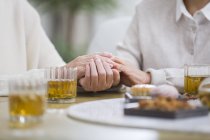 Cropped view of senior women holding hands while drinking tea — Stock Photo