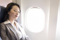 Chinese businesswoman resting on seat on flight — Stock Photo