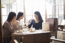 Mulher chinesa demonstrando novas roupas para amigos do sexo feminino no café — Fotografia de Stock