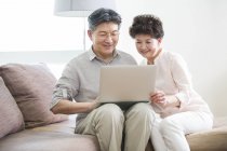 Senior couple chinois en utilisant un ordinateur portable sur le canapé — Photo de stock