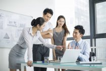 Equipo de negocios chino hablando en reunión y apuntando a la computadora portátil - foto de stock