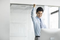 Homme d'affaires chinois acclamant et frappant l'air à l'ordinateur dans le bureau — Photo de stock