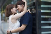 Young Chinese couple leaning on shop window and embracing on street — Stock Photo