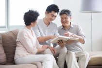 Chinese senior parents and adult son looking at photo album — Stock Photo