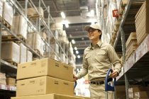 Male Chinese warehouse worker pushing boxes — Stock Photo