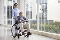 Infermiera cinese spingendo uomo anziano in sedia a rotelle — Foto stock