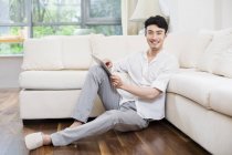 Hombre chino usando tableta digital en el suelo en la sala de estar - foto de stock