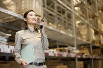 Female Chinese warehouse worker using walkie-talkie with clipboard — Stock Photo
