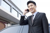 Chinese businessman talking on phone in front of car — Stock Photo