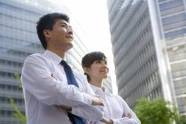 Chinese businessman and businesswoman with arms crossed in front of skyscraper — Stock Photo