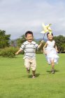 Irmãos chineses correndo com pinwheel no prado — Fotografia de Stock