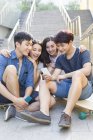 Amis chinois regardant smartphone sur les escaliers avec planches à roulettes — Photo de stock