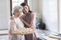 Chinese senior and young women making dumplings in kitchen — Stock Photo