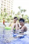 Chinese couple relaxing in hotel pool and looking in camera — Stock Photo