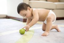 Chinese baby boy crawling and playing with green apple on carpet — Stock Photo