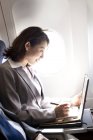 Femme d'affaires chinoise utilisant un ordinateur portable dans l'avion — Photo de stock