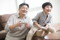 Avô e neto chineses jogando videogame na sala de estar — Fotografia de Stock