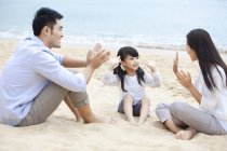 Genitori cinesi con figlia seduta e mani battenti sulla spiaggia — Foto stock