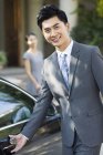 Giovane uomo d'affari cinese apertura porta auto con donna in background — Foto stock