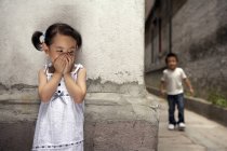 Menina chinesa cobrindo boca enquanto joga esconder e procurar — Fotografia de Stock