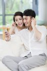 Молодая китайская пара слушает музыку со смартфоном на диване дома — стоковое фото