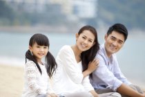 Chinese parents with daughter resting on beach sand and looking in camera — Stock Photo