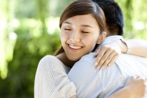 Joven mujer china abrazando novio en parque - foto de stock