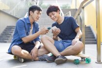 Китайцы сидят на скейтбордах и смотрят на смартфоны — стоковое фото
