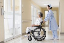Китайская медсестра ухаживает за пожилой женщиной в инвалидном кресле — стоковое фото