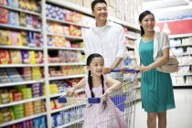 Padres chinos con hija en el carrito de compras en el supermercado - foto de stock