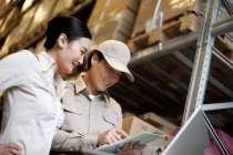 Chinese businesswoman in warehouse with workers using a laptop — Stock Photo