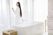 Chinese woman in bathrobe standing by bathroom window — Stock Photo