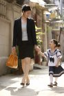 Chinese schoolgirl walking with mother on street — Stock Photo