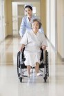 Enfermera china empujando a una mujer mayor en silla de ruedas - foto de stock