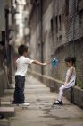 Китайский мальчик дает грустной девушке бумажную ветряную мельницу в переулке — стоковое фото