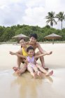 Китайская семья с девочкой с протянутыми руками сидит на пляже — стоковое фото