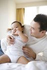 Cinese uomo holding infantile figlio su letto — Foto stock